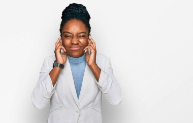 Genç Afro-Amerikalı kadın iş kıyafetleri giyip kulaklarını parmaklarıyla kapatıyor ve yüksek sesli müzik sesi için rahatsız edici bir ifade takınıyor. sağır kavramı. 