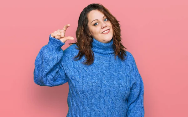 Genç ve cüsseli bir kadın günlük kıyafetler giyiyor gülümsüyor ve el hareketleriyle küçük beden işaretleri yapıyor parmaklarıyla bakıyor ve kameraya bakıyor. ölçüm kavramı. 