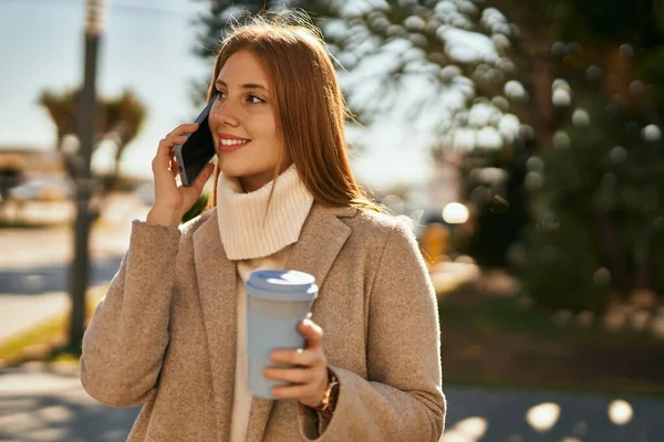 Genç kızıl saçlı kız akıllı telefonda konuşuyor. Şehirde kahve içiyor..