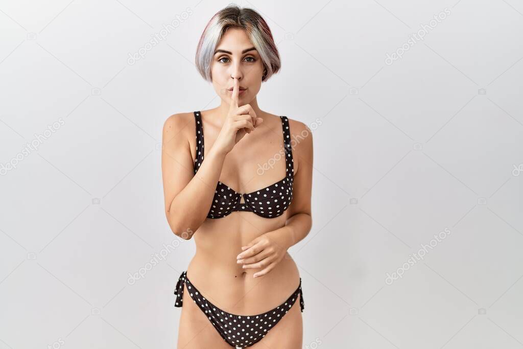 Young beautiful woman wearing swimsuit over isolated background asking to be quiet with finger on lips. silence and secret concept. 