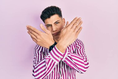 Gündelik kıyafetler giyen genç İspanyol adam. Reddedilmiş yüz ifadesi. Kollar ve avuçlar çapraz. 