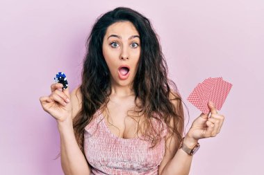 Elinde kumarhane fişleri ve kartlarıyla poker oynayan genç İspanyol kadın şaşkınlık ve şaşkınlık dolu bir ifade, korku ve heyecan dolu bir yüz ifadesiyle dehşete düştü.. 