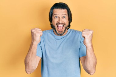 Orta yaşlı, günlük kıyafetler giyen beyaz bir adam kollarını kaldırıp, gözleri açık bir şekilde başarıyı kutluyor. Kazanan konsept. 