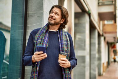 Orta yaşlı yakışıklı adam akıllı telefon kullanıyor. Kasabada kahve içiyor.