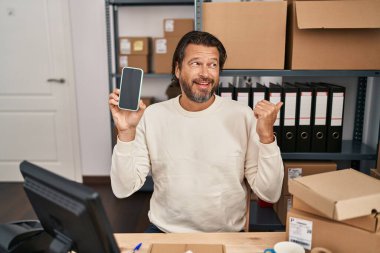 Küçük işletme şirketinde çalışan yakışıklı, orta yaşlı bir adam elinde akıllı bir telefonla baş parmağını kaldırıyor ve ağzı açık gülümsüyor. 