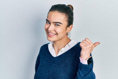 Kafkasyalı genç bir kız, günlük kıyafetler giyiyor, gülümsüyor, gülümsüyor ve başparmağıyla yan tarafa bakıyor.. 