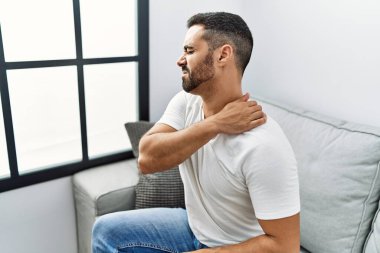 Genç İspanyol adam boynuna dokunuyor. Evde sırt ağrısı çekiyor.