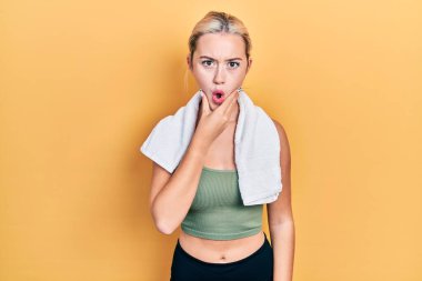 Spor kıyafetleri ve havlu giyen genç sarışın kız, elleri çenesinde, inanamama, şaşkınlık ve şaşkınlık dolu bir ifade takınıyor. 