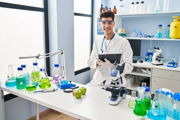 Laboratuvarda panoya yazı yazan, bilim adamı üniforması giyen İspanyol bir genç.