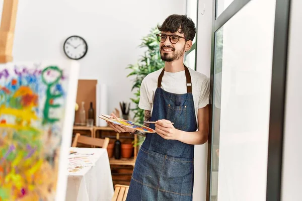 Genç İspanyol ressam mutlu bir şekilde resim stüdyosunda duruyor..