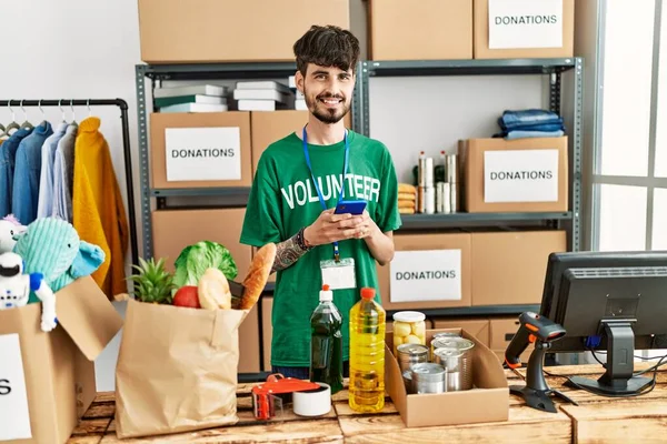 Young Hispanic Man Wearing Volunteer Uniform Usong Smartphone Charity Center — Stok fotoğraf