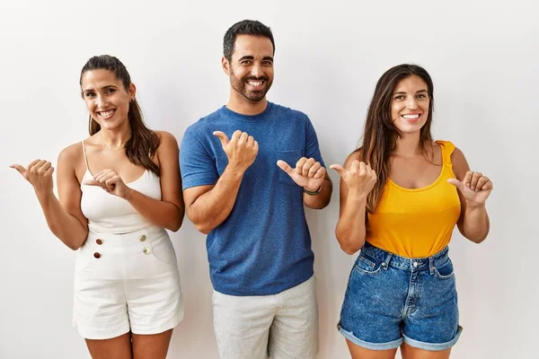 Bir grup İspanyol genç, izole edilmiş arka planda durup elleri ve başparmakları havada, kendinden emin gülümseyen insanları işaret ediyor. 