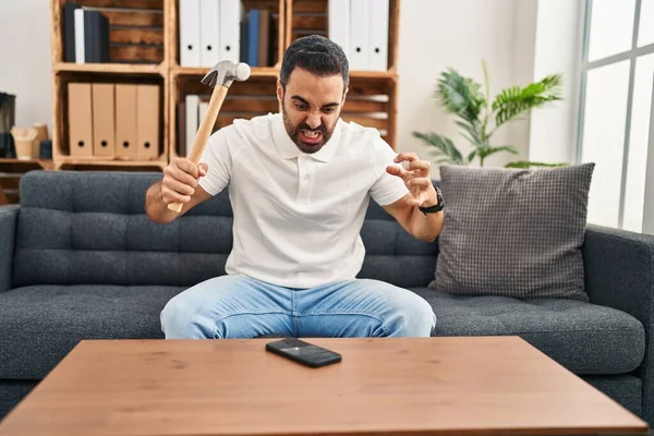 Young Hispanic Man Stressed Breaking Smartphone Hammer Home — Stockfoto