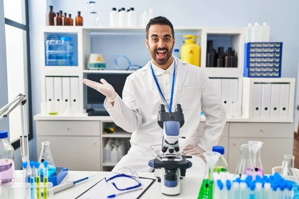 Laboratuvarda çalışan, sakallı, neşeli gülümseyen, elinde avucuyla kameraya bakan genç İspanyol bir adam.. 