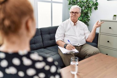 Muayenehanedeki kıdemli psikolog yüzünde kocaman bir gülümsemeyle kameraya el ile işaret ederek bakıyor.. 