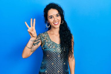Bindi ve geleneksel kurta elbisesi giyen genç bir kadın üç numarayı gösterip işaret ederken kendinden emin ve mutlu bir şekilde gülümsüyor.. 