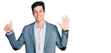 İş kıyafetleri giymiş genç İspanyol adam kendini beğenmiş ve mutlu bir şekilde gülümserken altı numarayı gösterip işaret ediyor.. 