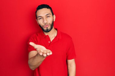 Sakallı, sıradan kırmızı tişörtlü İspanyol bir adam kameraya bakıp havada el sallayarak öpüşüyor ve güzel ve seksi oluyor. aşk ifadesi. 