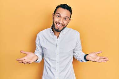 Sakallı, iş gömleği giyen, kafası karışmış, elleri ve kolları havada İspanyol bir adam. şüphe kavramı. 