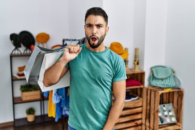 Satış mağazasında sakallı genç ve yakışıklı bir adam. Şok olmuş bir halde. Şüpheci ve alaycı görünüyor. 