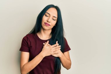 Gündelik tişört giyen genç İspanyol kız elleri göğsünde gülümsüyor, gözleri kapalı ve yüzünde minnet ifadesi var. sağlık kavramı. 