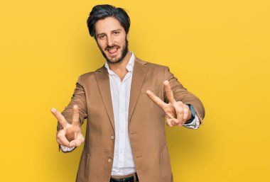 İş kıyafetleri giymiş, ağzı açık gülümseyen genç bir İspanyol zafer işareti yaparken parmaklarını gösteriyor. İki numara.. 