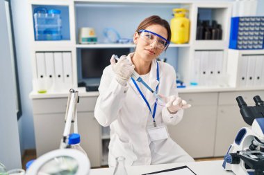 Laboratuvarda pipet kullanan, bilim adamı üniforması giyen İspanyol genç bir kadın.