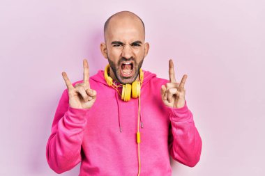 Spor kıyafetleri giymiş, kulaklık takmış çılgın bir ifadeyle bağıran kel bir adam elleri havada rock sembolü yapıyor. Müzik yıldızı. ağır kavram. 