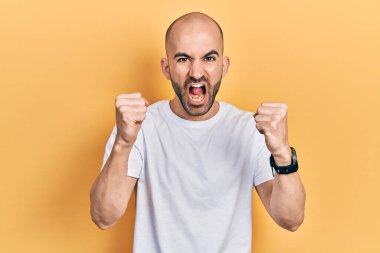 Kızgın ve kızgın beyaz tişört giyen genç kel bir adam öfkeyle bağırırken sinirli ve öfkeli yumruklar sallıyor. öfke ve agresif konsept. 