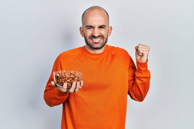 Fıstık tutan genç kel adam gururla bağırıyor, zaferi kutluyor ve başarıyı kollarını kaldırarak kutluyor. 