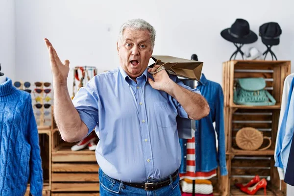 Gri saçlı son sınıf öğrencisi mağazada alışveriş torbaları tutuyor zaferi kutluyor mutlu bir gülümseme ve ellerini kaldırarak kazanan bir ifadeyle. 