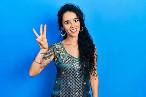 Bindi ve geleneksel kurta elbisesi giyen genç bir kadın üç numarayı gösterip işaret ederken kendinden emin ve mutlu bir şekilde gülümsüyor.. 