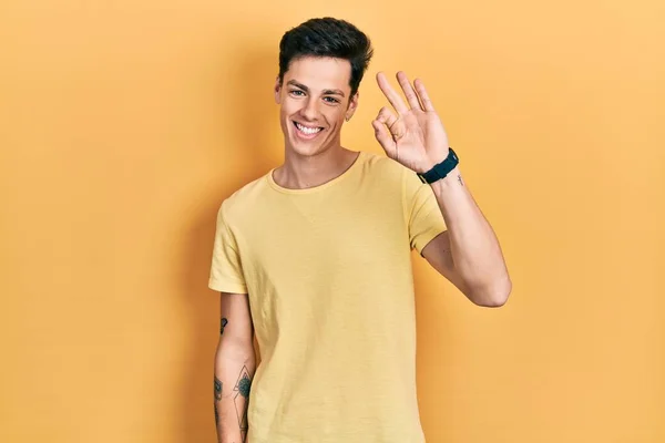 Młody Hiszpan Żółtej Koszulce Uśmiecha Się Pozytywnie Robiąc Znak Dłońmi — Zdjęcie stockowe