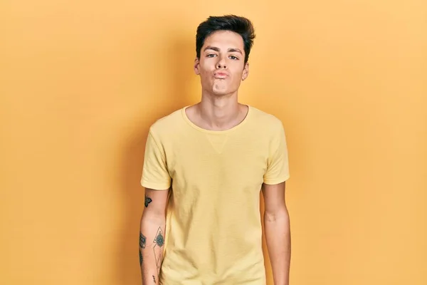 Young Hispanic Man Wearing Casual Yellow Shirt Looking Camera Blowing — Stockfoto