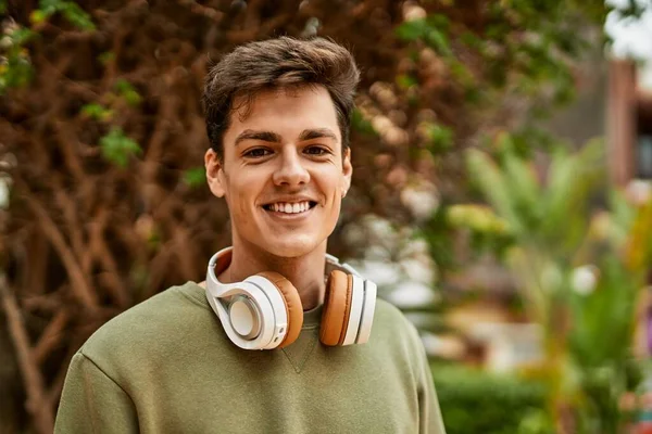 Şehirde kulaklık takarak mutlu gülümseyen genç İspanyol adam..