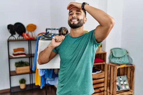 Satış mağazasında sakallı, alışveriş torbaları tutan, kendine güvenen, el hareketleriyle saçlara dokunan çekici ve şık görünümlü genç bir adam. 