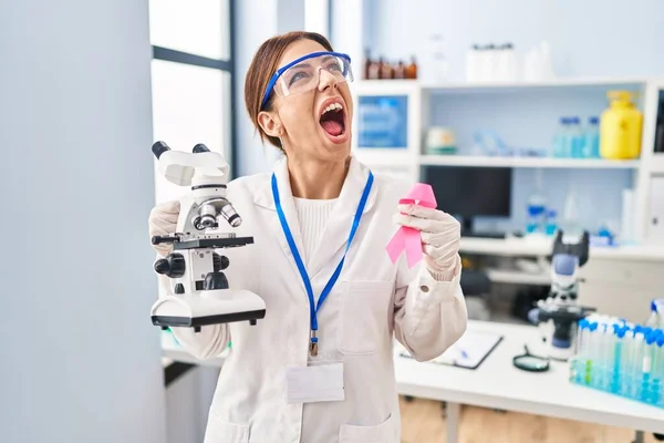 Young Brunette Woman Working Scientist Laboratory Holding Pink Ribbon Angry — Stockfoto