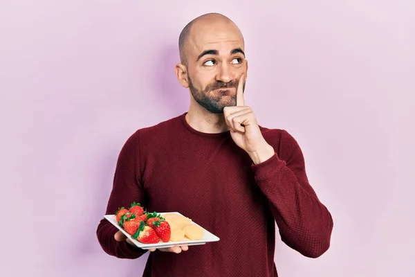 Young Bald Man Eating Fresh Healthy Fruits Serious Face Thinking — Stock Photo, Image