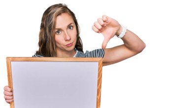 Kızgın yüzlü, boş beyaz tahta tutan genç sarışın kadın, olumsuz işaret baş parmakları aşağıda, reddedilme konsepti 