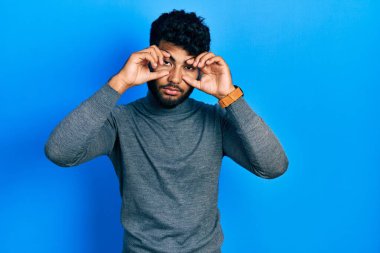 Balıkçı yaka kazak giyen Arap adam gözlerini parmaklarıyla açmaya çalışıyor, uykulu ve yorgun. 