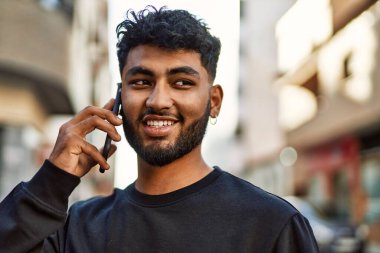 Genç Arap adam gülümsüyor, kendinden emin bir şekilde caddedeki akıllı telefondan konuşuyor.