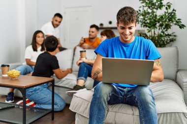 Kanepede mutlu bir şekilde oturan bir grup genç arkadaş. Evde dizüstü bilgisayar kullanan bir adam.