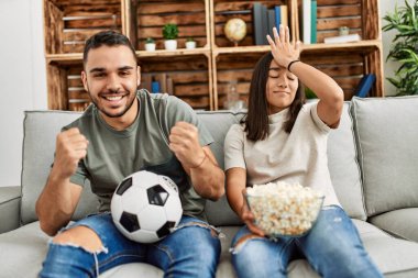 Genç latin çift evde futbol maçı izleyip porpcorn yiyorlar..