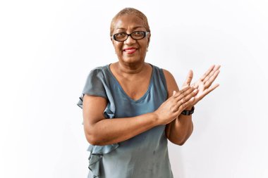 Mature hispanic woman wearing glasses standing over isolated background clapping and applauding happy and joyful, smiling proud hands together 