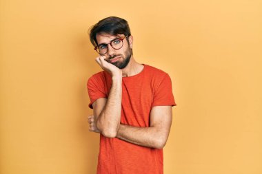 Gündelik kıyafetler ve gözlük takan genç İspanyol adam çapraz kollu depresyondan sıkılmış ve yorgun göründüğünü düşünüyor.. 