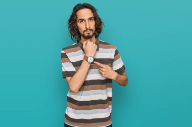 Gündelik kıyafetler giyen genç İspanyol adam saati, sabırsızlığı ve rahat bir ifadeyle kameraya bakmayı işaret ediyor. 