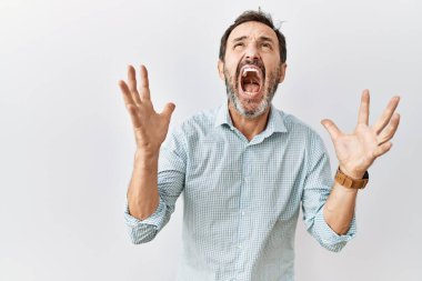 Orta yaşlı, sakallı bir İspanyol adam izole bir arka planda çılgın ve kızgın bir şekilde bağırıyor ve agresif bir ifade ve kolla bağırıyor. hüsran kavramı. 