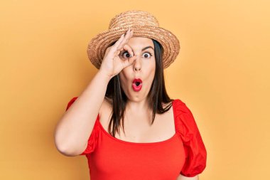 Yaz şapkası takan genç İspanyol kadın şaşırmış yüz ifadesiyle şaşırmış, parmaklarından içeri bakıyor. İnançsız ifade. 