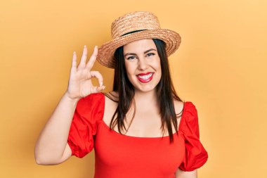 Yaz şapkası takan genç İspanyol kadın olumlu gülümsüyor ve el ve parmaklarıyla 