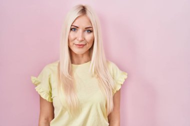 Pembe arka planda duran beyaz kadın yüzünde ciddi bir ifadeyle rahatlamış. Basit ve doğal bir şekilde kameraya bakıyorsun.. 